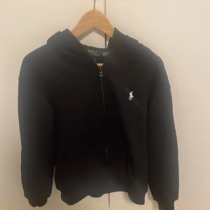 Svart hoodie från Ralph Lauren - Säljer en stilren svart hoodie från Ralph Lauren med dragkedja och det klassiska logotypbroderiet på bröstet. Perfekt för en avslappnad och trendig look. 🖤