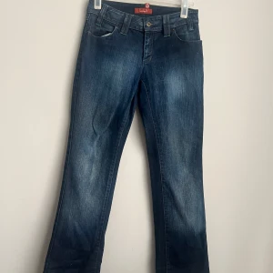 Vintage Blå jeans med gröna detaljer - Snygga blå jeans från VM med gröna sömmar på bakfickan. Klassisk femficksdesign och knappgylf. Perfekta för en avslappnad stil.