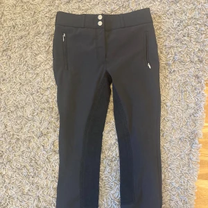 Svarta ridbyxor från CRW - Snygga svarta ridbyxor från CRW med medel hög midja och dragkedjor vid fickorna. Byxorna har en tight passform och är perfekta för ridning. De har även knappar i midjan för extra säkerhet. Dom är fodrade så passar bäst på vintern