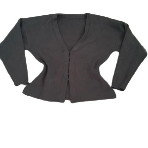 Mörk grå kofta med v-ringning - Säljer en stilren svart kofta med v-ringning och långa ärmar. Perfekt för lager-på-lager och enkel att matcha med olika outfits. Koftan har en klassisk design med speciella knappar framtill.