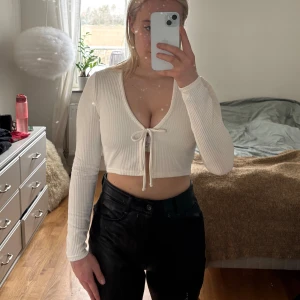 Vit ribbad croppad topp - Säljer en stilren vit ribbad topp med lång ärm och knytning framtill. Toppen är croppad och har en v-ringad design som ger en trendig look.