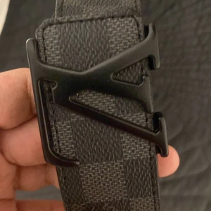 Svart och grått bälte med rutigt mönster - Snyggt bälte med ett svart och grått rutigt mönster och en unik svart spänne. Perfekt för att ge din outfit en stilren touch.