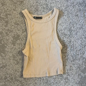 Beige ribbad linnetopp från Zara - Säljer en stilren beige ribbad linnetopp från Zara. Perfekt för varma dagar med sin ärmlösa design och bekväma passform. Enkelt att matcha med olika outfits! Från Zara i storlek xs använt fåtal gånger 