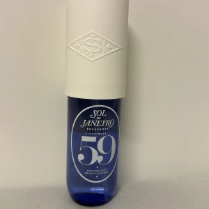 Sol de Janeiro Cheirosa 59 Perfume Mist - Fräsch och upplyftande doft från Sol de Janeiro, Cheirosa 59. Flaskan är blå med en vit kork och har en elegant design. Doften innehåller toner av vanilj, orkidé, viol och sandelträ, vilket ger en varm och inbjudande känsla. Endast testad. 