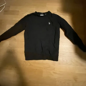 Svart tröja från U.S. Polo Assn. - Säljer en stilren svart tröja från U.S. Polo Assn. med ett diskret logotypbroderi på bröstet. Tröjan har långa ärmar och en klassisk rund halsringning. Perfekt för en avslappnad och snygg look.