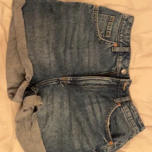 Blå jeansshorts från H&M - Snygga blå jeansshorts från H&M med klassisk femficksdesign och uppvikta ben. Perfekta för en avslappnad sommarlook. De har en knapp och dragkedja framtill.