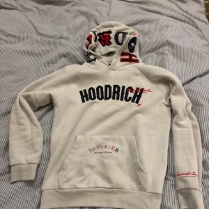  Hoodrich - Säljer en vit hoodie från Hoodrich med tryck både fram och bak. Den har en stor ficka framtill och textdetaljer på huvan. Perfekt för en avslappnad stil.