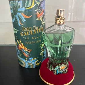 Jean Paul Gaultier Le Beau Paradise Garden - Säljer en exklusiv parfym från Jean Paul Gaultier, 'Le Beau Paradise Garden'. Den har inte används mycket gånger eftersom jag har andra. Flaskan har en unik design i form av en manlig torso i grönt glas med guldiga detaljer. Förpackningen är färgglad med tropiska mönster och texten 'Paradise Garden'. Perfekt för den som vill ha en doft med karaktär och stil.