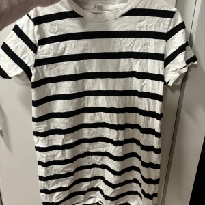 Randig t-shirt från H&M - Säljer en klassisk svartvit randig t-shirt klänning från H&M. Den är kortärmad och gjord i mjuk bomull. Går ju att ha som en over size T-shirt också! Lite skrynklig då den bara hängt i garderoben och aldrig använts.