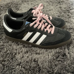 Adidas Samba OG sneakers  - Säljer mina tvärfeta Adidas Samba OG sneakers storlek 43. Skorna har den klassiska svarta färgen och jag själv har valt att sätta i rosa skosnören för en unik look. SVARTA SKOSNÖREN MEDKOMMER dock! Skorna är i väldigt bra skick och bara använda ett fåtal gånger, perfekta inför våren och sommaren! Tveka inte att höra av er vid frågor eller ytterligare bilder, priset är inte hugget i sten! 