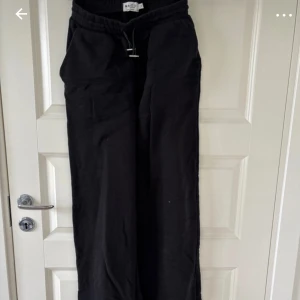 Svarta byxor från NA-KD - Säljer ett par svarta byxor från NA-KD med elastisk midja i storlek S. Bakfickorna går inte att öppna!                                                          Midjemått rakt över: 32cm                                     Innerbenslängd: 73cm                                              Hela benet: 105cm