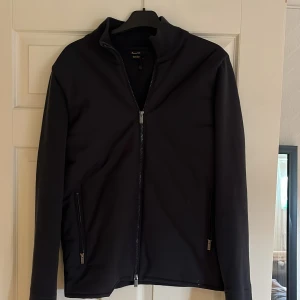 Mörkblå cardigan  från Massimo Dutti - Säljer en stilren cardigan  från Massimo Dutti med dragkedja framtill. Jackan har en ribbad krage och långa ärmar, perfekt för en snygg och enkel look. Jag är 182cm lång