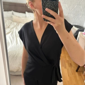 Superfin Zara topp - Snygg svart omlottopp från Zara med knytning i midjan. Perfekt för en stilren look. Toppen har en v-ringad design och korta ärmar🤍