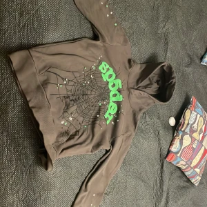 Sp5der puff print hoodie - Cool brun hoodie från Sp5der med ett stort grönt tryck och spindelnätsdesign på framsidan. Tröjan har långa ärmar med små stjärnor och en klassisk huva. Perfekt för en avslappnad stil. Vid snabb affär kan priset sänkas 