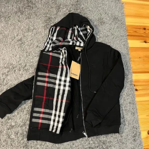 Burberry Zip Hoodie Svart - Helt ny burberry zip hoodie. Säljs pga den inte kommer till användning. 10/10 skick, inga skador eller liknande. Det är storlek L men den passar även M. Riktigt skönt material och väldigt fin. Rekommenderar starkt!