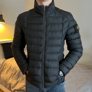 Stone Island jacka SMALL - Säljer en stilren svart dunjacka från stone island. Jackan har en hög krage och dragkedja framtill. Den ikoniska stone island-loggan sitter på ärmen. Perfekt för vår, höst, men även kyliga sommarkvällar. Den är i utmärkt skick och med väldigt god kvalite, men det låga priset beror på ett skrapmärke på den högra axeln (se sista bilden). Det är inget som märks särsklit mycket, men det syns ju fortfarande. Mvh/ gustav