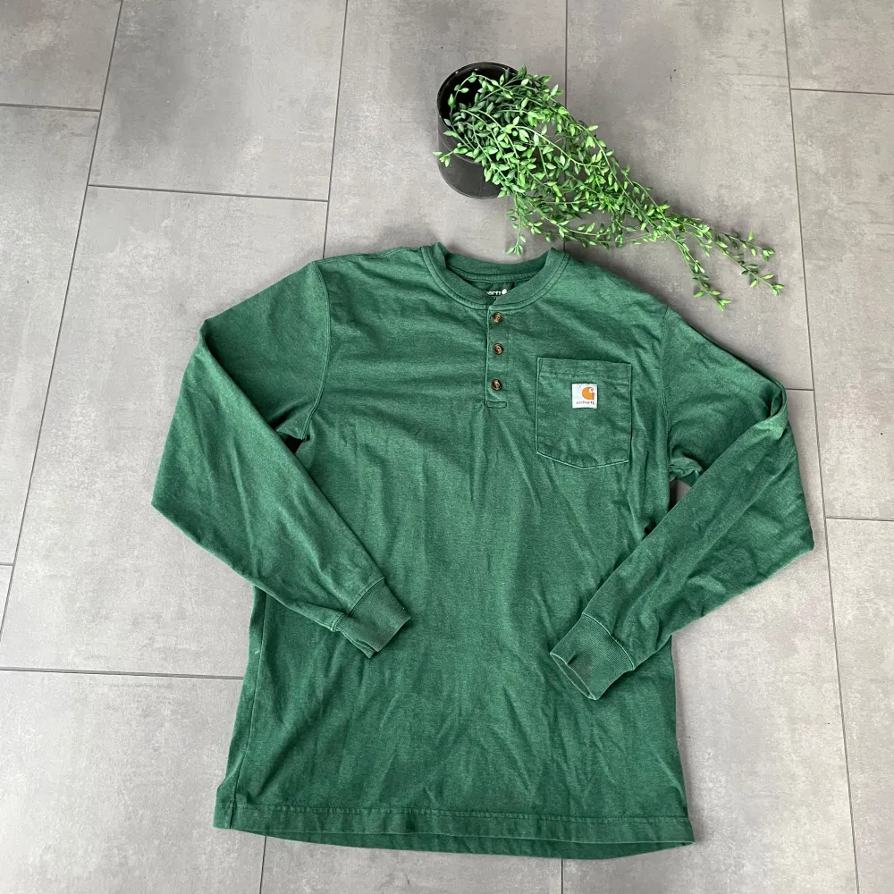 Säljer en Carhartt långärmad Henley-tröja i en snygg grön färg. Tröjan är i mycket bra skick, knappt använd. Storlek M med loose fit för en avslappnad och bekväm passform. ✔️ Mjukt och slitstarkt material ✔️ Klassisk Henley-design med tre knappar ✔️ Bröstficka med Carhartt-logga Perfekt för vardagsbruk eller lager-på-lager-stil! Skickas snabbt efter köp. Hör av dig vid frågor!. Neuletakit & Villapaidat.