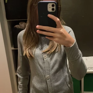 Grå hoodie från Sail Racing - Säljer en grå hoodie från Sail Racing med knappar framtill. Tröjan har långa ärmar och ribbade muddar vid ärmslut och nederkant. Perfekt för en avslappnad stil. Har detaljer på luvan!!Hör av dig vid intresse!