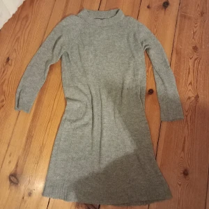 Grå stickad klänning från 157 - Säljer en mysig grå stickad klänning från 157. Klänningen har långa ärmar och en enkel design som passar perfekt för kyligare dagar. Perfekt för att hålla sig varm och stilren. 103cm lång.