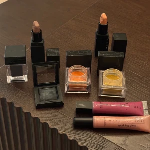 Makeupstore smink - Ett sminkset från Make Up Store med två läppstift i nude och kopparfärger, två ögonskuggor i orange och gul, samt två läppglans i rosa och persikofärger. Perfekt för att skapa en färgglad look.