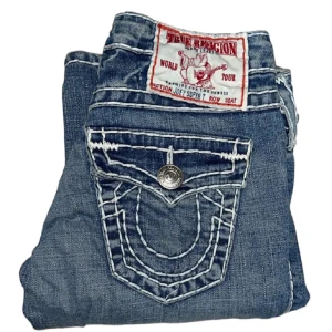True Religion Jeans - Snygga lågmidjade bootcut/flare jeans från True Religion med klassisk femficksdesign och dekorativa sömmar på bakfickorna. Inga defekter förutom smått slitna längst ner på byxbenen. [Midjemått: 36cm] [Innerbenslängd: 82cm] Skriv om du har några funderingar!