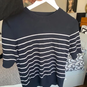 Mörkblå randig tröja från 157 - Säljer en stilren mörkblå tröja med vita ränder från 157. Tröjan har korta ärmar och en rund halsringning. Perfekt för en avslappnad look.