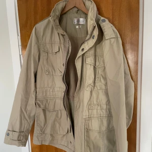 Beige field jacka från These Glory Days - En perfekt field jacka från These glory days i storlek s. flera fickor, dragkedja och knappar framtill. Nypris Långås 2500kr. Den har en hög krage och en luva man kan ta fram. Perfekt för vår och höst! Meetup i Stockholm eller frakt mot betalning. 
