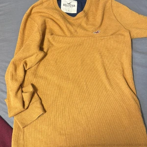 Gul långärmad tröja från Hollister - Säljer en snygg gul långärmad tröja från Hollister. Tröjan har en liten logga på bröstet och är tillverkad i ett bekvämt material. Perfekt för en avslappnad stil. Hör av dig vid intresse! 🌟