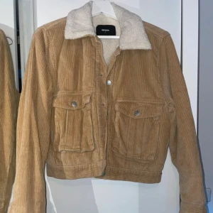 Beige manchesterjacka från Bik Bok - Säljer en snygg beige manchesterjacka från Bik Bok med mjukt teddyfoder i kragen. Jackan har knappar framtill och två fickor med knappstängning. Använd fåtal gånger 