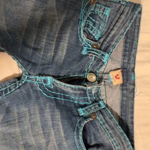 True religion  - Säljer dessa extremt unika true religion jeans med turkos sömmar. Dem säljs inte längre. Finns defekter se bilder men dem märks inte så mycket på. Midjemått 38, inrebenlängd 86, utsvängda och lågmidjade