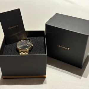 Guld klocka från GANT - Elegant guldarmbandsklocka från GANT med svart urtavla. Klockan har en stilren design och kommer i originalförpackning klockan är oanvänd och är helt ny. Den här klockan är perfekt för dig som satsar på en mer stilren och exklusiv look! Det följer även med extra länkar för att kunna justera storleken efter just din handled. När klockan köptes i afär så kostade den runt 2600kr. Jag säljer klockan för 999!!!