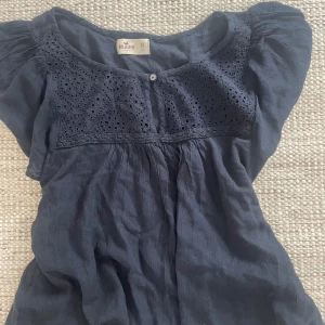 Mörkblå blus från Hollister - Säljer en söt mörkblå blus från Hollister med broderade detaljer och en knapp framtill. Har nästan aldrig kommit till användning!💗