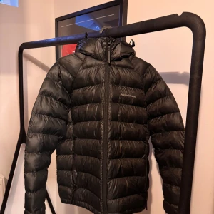 Svart dunjacka från Peak Performance - Säljer en svart dunjacka från Peak Performance. Jackan har en dragkedja framtill och är långärmad med en huva. Perfekt för kyligare väder. Stl 170 men passar S/XS