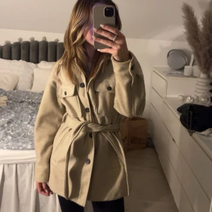 Beige kappa med bälte - Snygg beige kappa med bälte och knappar framtill. Perfekt nu till våren, men kan även användas till hösten 🤩 Använd ett par gånger bara så den är i väldigt fint skick! Rökfritt hem