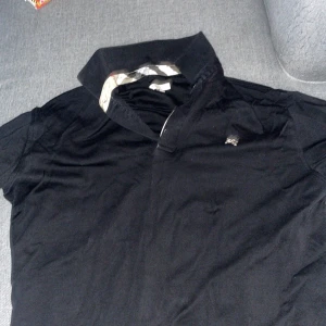 Svart pikétröja från Burberry - Snygg svart pikétröja från Burberry med klassisk krage och diskret logga på bröstet. Perfekt för en stilren look.