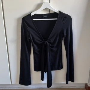 Svart långärmad topp med knyt - Snygg svart långärmad topp från Gina Tricot med v-ringning och knyt framtill. Perfekt för en stilren look.