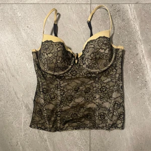 Svart spetskorsett - Elegant svart korsett med spetsdetaljer och justerbara axelband. Den har en vacker blommig spetsdesign och en beige bas🥰i 80B, stretchig material 