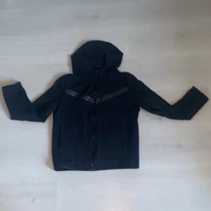 Svart huvjacka från Nike - Säljer en stilren svart huvjacka från Nike med dragkedja framtill. Jackan har långa ärmar och en praktisk huva. Perfekt för en sportig look eller avslappnade dagar. 🖤
