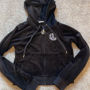 Svart kofta från Juicy Couture - Säljer en svart hoodie från Juicy Couture i mjuk sammet med dragkedja och huva. Den har ett snyggt emblem på bröstet och ryggen. (Är en äldre variation men är äkta)