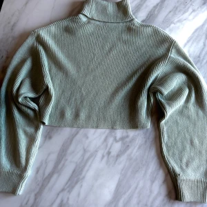 Grön ribbad croppad polotröja - Snygg grön croppad polotröja med ribbad struktur. Perfekt för en trendig look med långa ärmar och hög krage. Passar utmärkt till både jeans och kjol. 