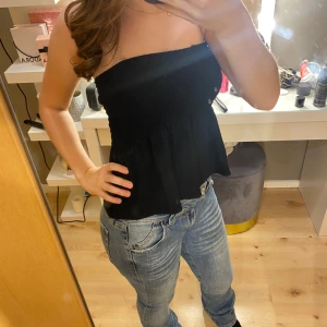 Svart tubtopp - Säljer en stilren svart tubtopp med en luftig passform. Perfekt för varma dagar eller som en del av en lager-på-lager-look. Toppen är ärmlös och har en lätt volangdetalj vid nederkanten.