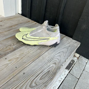 Nike fotbollsskor i gult och grått - Snygga fotbollsskor från Nike i en fräsch gul och grå färgkombination. Skorna har en modern design med mönstrad ovandel och svarta detaljer. Perfekta för fotbollsplanen med sina greppvänliga dobbar.