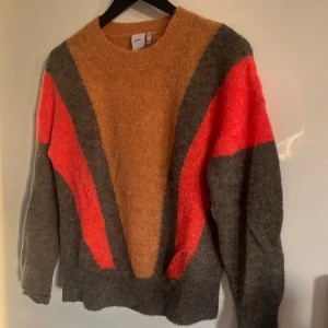 Stickad tröja från ICHI - Säljer en cool stickad tröja från ICHI i storlek S. Tröjan har ett unikt mönster i orange, grått och rött med långa ärmar. Perfekt för att liva upp garderoben!