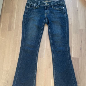 Blå bootcut jeans med broderade fickor - Snygga blå lågmidjade bootcut jeans med unika broderade detaljer på bakfickorna. Säljer för att den inte passar mig längre