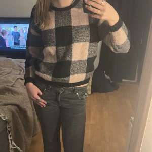 Rutig stickad tröja i svart och beige - Säljer en mysig stickad tröja med ett stort rutmönster i svart och beige. Tröjan har långa ärmar och en rund halsringning. Perfekt för kyligare dagar!
