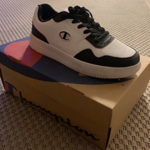 Svartvita sneakers från Champion - Snygga svartvita sneakers från Champion med klassisk design. Skorna har snörning och en stilren logga på sidan. Perfekta för en casual look. Storlek 40