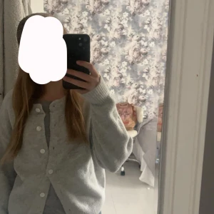 Ljusgrå kofta med knappar - Säljer en mysig ljusgrå kofta med knappar framtill. Perfekt för kyliga dagar och lätt att matcha med olika outfits. Koftan har långa ärmar och en klassisk design.