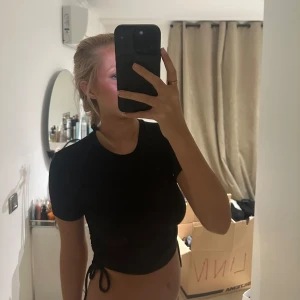 Svart kortärmad topp med dragsko på sidorna - Säljer en svart kortärmad topp med dragsko i sidan.  Där man själv kan välja hur kort eller lång man vill att toppen ska vara. Perfekt för en stilren look. Från Zara