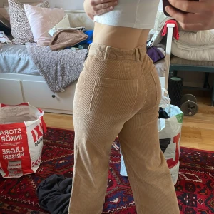 Beige manchesterbyxor - Snygga beige manchesterbyxor med hög midja och vida ben. Byxorna har klassiska fickor och knäppning fram. Perfekta för en trendig och avslappnad stil.