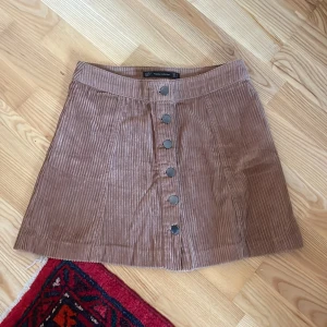 Brun manchesterkjol med knappar - Snygg brun manchesterkjol från zara i storlek S Kjolen har en rad med knappar framtill och en kort längd som ger en trendig look. Perfekt för att styla med en enkel topp eller tröja.